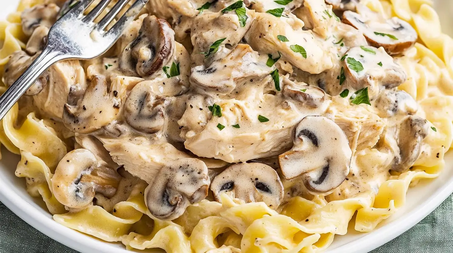 A plate of creamy mushroom chicken served over egg noodles, garnished with parsley.